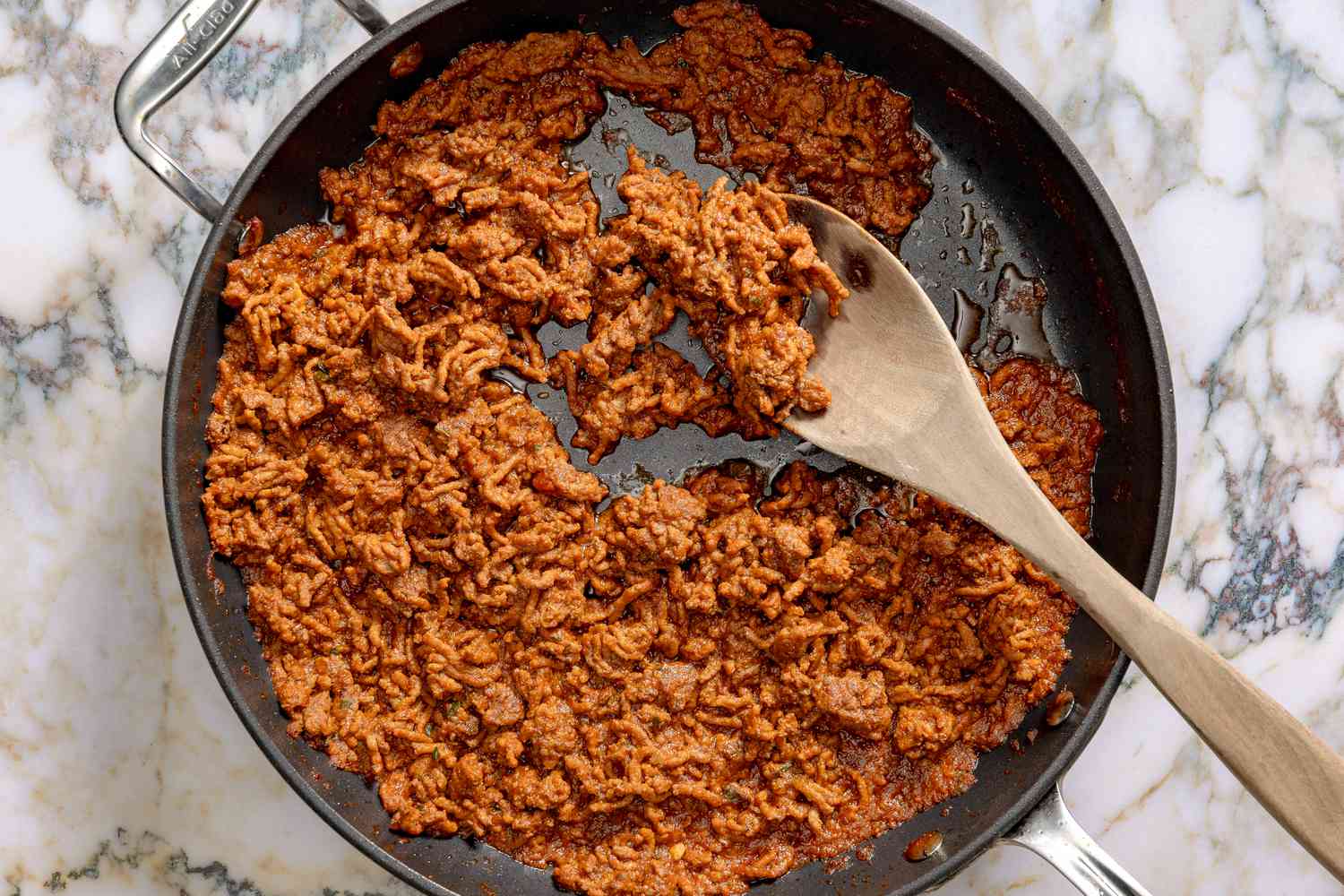 Overhead view of a wooden spoon in a skillet of ground beef, adobo and sazón mixture for Easy Puerto Rican Picadillo recipe