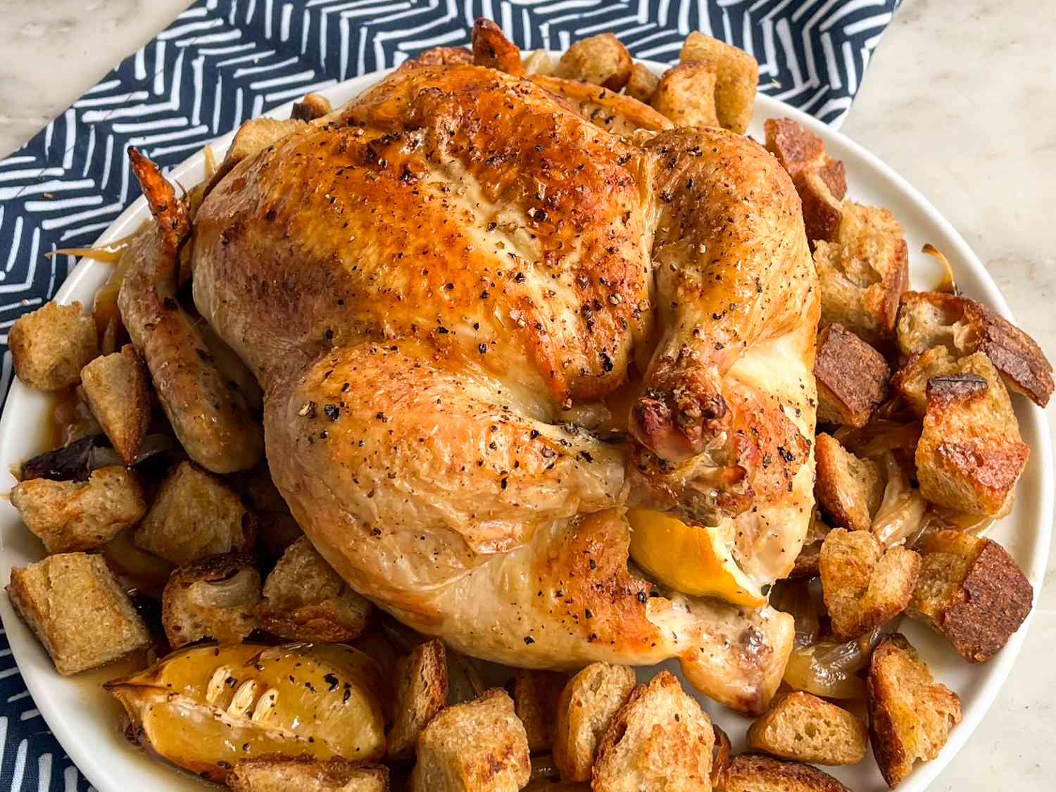 Roast chicken on a plate surrounded by croutons, ready for serving