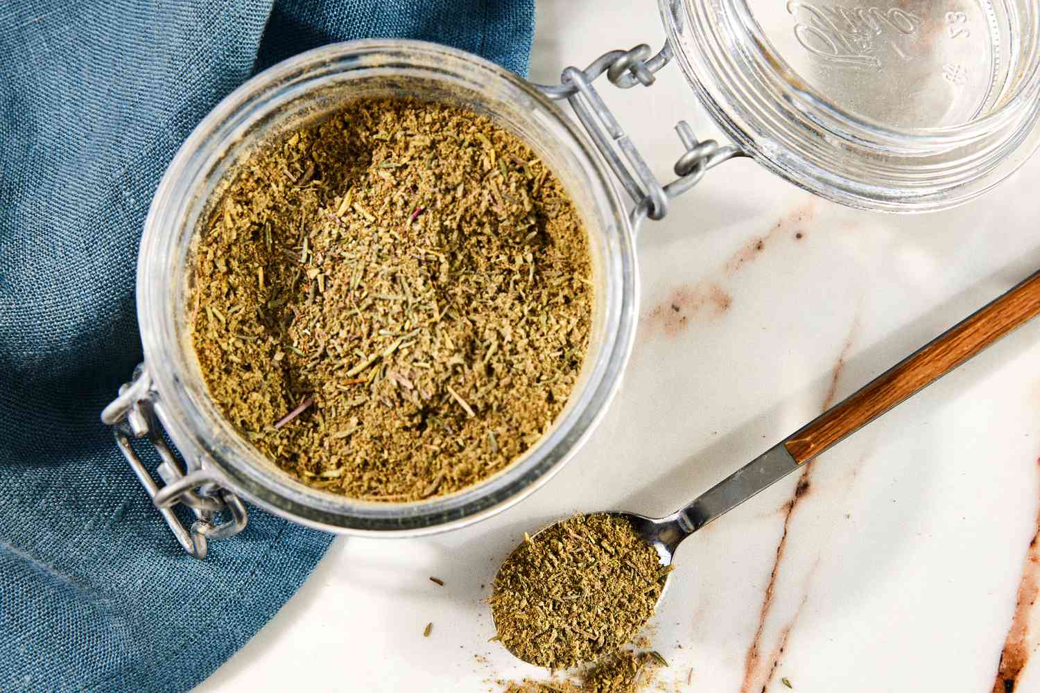 Jar of Poultry Seasoning With a Spoonful of Seasoning Next to a Navy Blue Table Napkin 