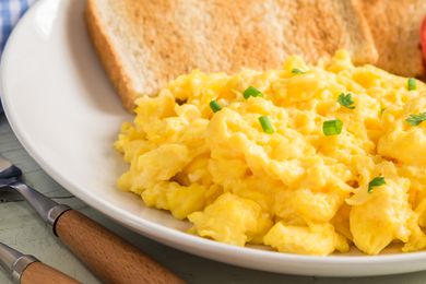 Close up of scrambled eggs topped with chives on a white plate next to pieces of toast