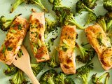 Roasted salmon fillets and broccoli on a tray with a wooden spatula