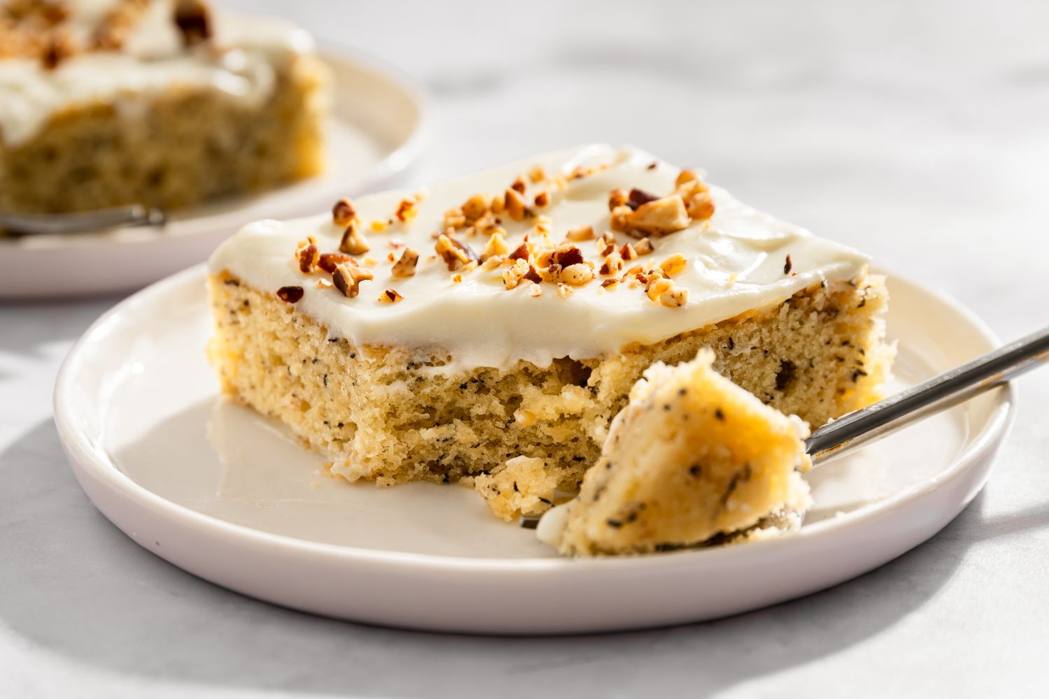 A banana dessert bar topped with cream cheese frosting and chopped nuts on a plate