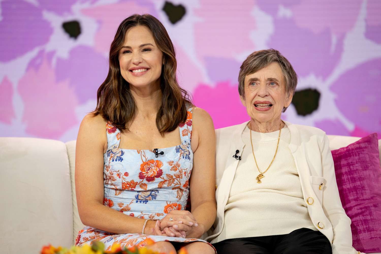 Two women seated together smiling indoors with a decorative background