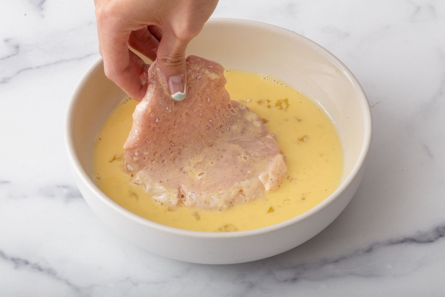 Dredging floured cutlet in egg mixture for a schnitzel recipe.