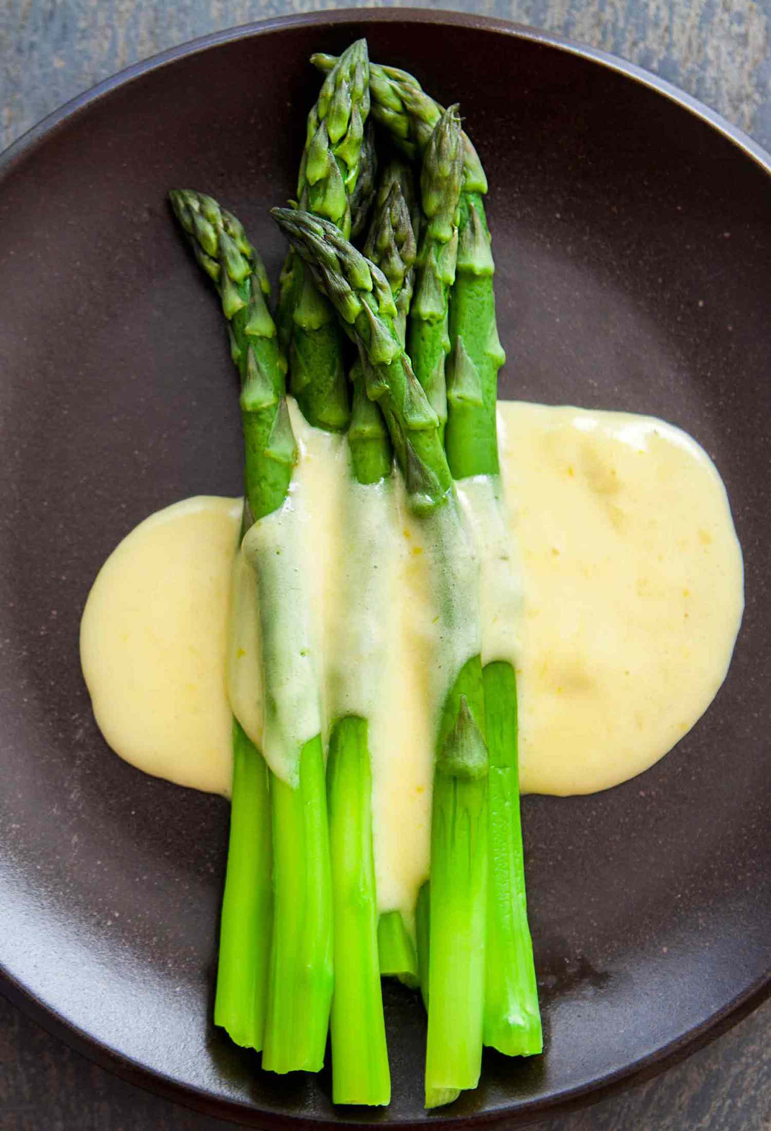 Steamed asparagus on a dark plate topped with Hollandaise sauce