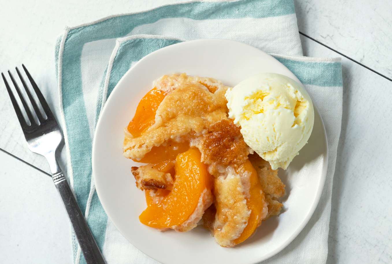 Peach cobbler served on a plate with a scoop of ice cream accompanied by a fork