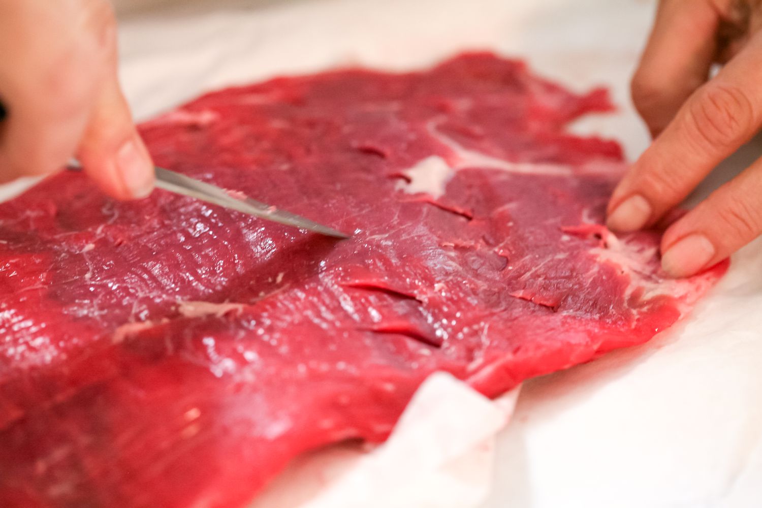 Cutting slits in raw flank steak.