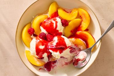 Bowl with sliced peaches, scoops of ice cream, raspberries, and red sauce