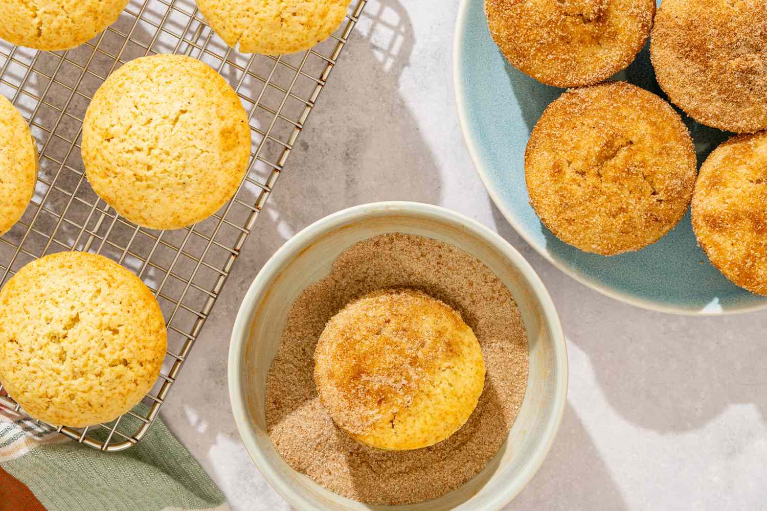 Old-Fashioned Donut Muffins, plain ones on a cooling rack, one in a cinnamon sugar mixture, coated ones on a plate