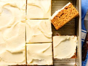 Sliced frosted carrot cake in a baking pan with one raised piece