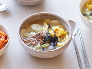A table set with a bowl of Dduk guk (Korean rice cake soup) and spoons.