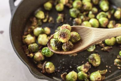 A wooden spoon scooping up roasted brussel sprouts in a cast iron pan.