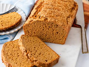 Angled view of a loaf of pumpkin bread on a marble cutting board with two slices in front and one on a plate to the side