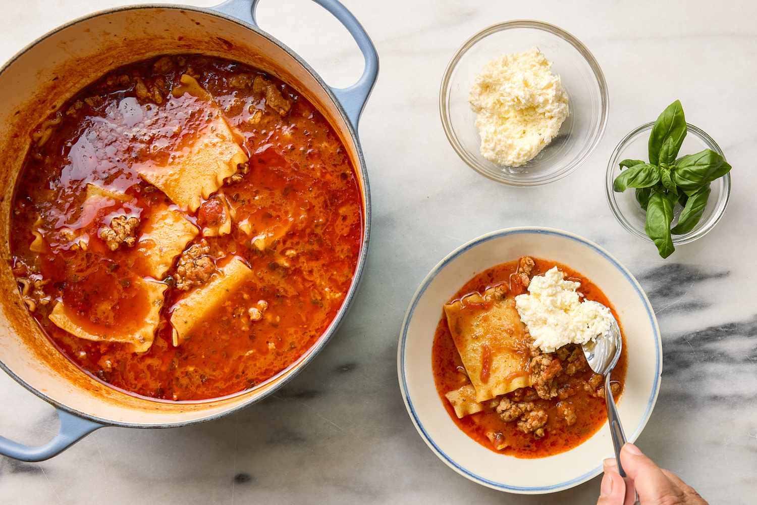 Pot and bowl of lasagna soup with ricotta and basil garnishes