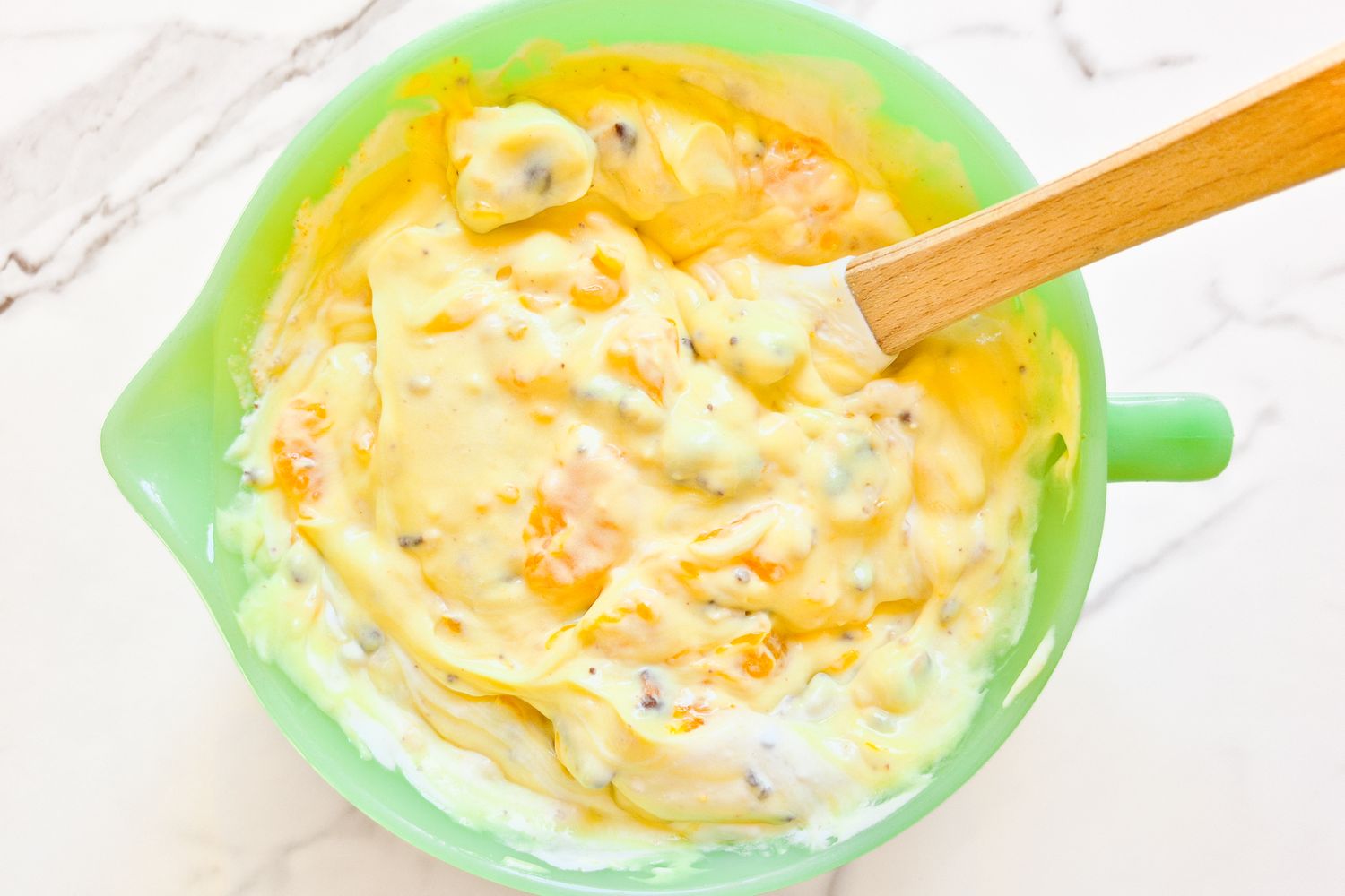 A green mixing bowl filled with a dessert mixture and a wooden spoon