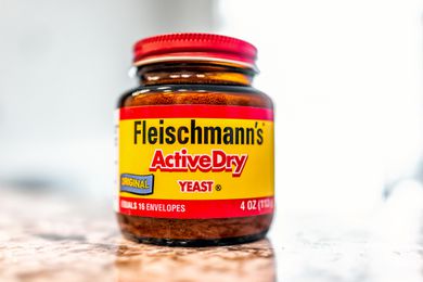Closeup front view of Fleischmann's Active Dry Yeast jar on a brown and white countertop with a gray background