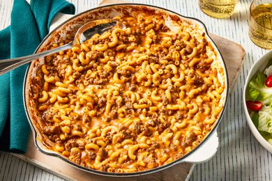 homemade hamburger helper in a skillet at a table setting with two glasses of soda and a side salad