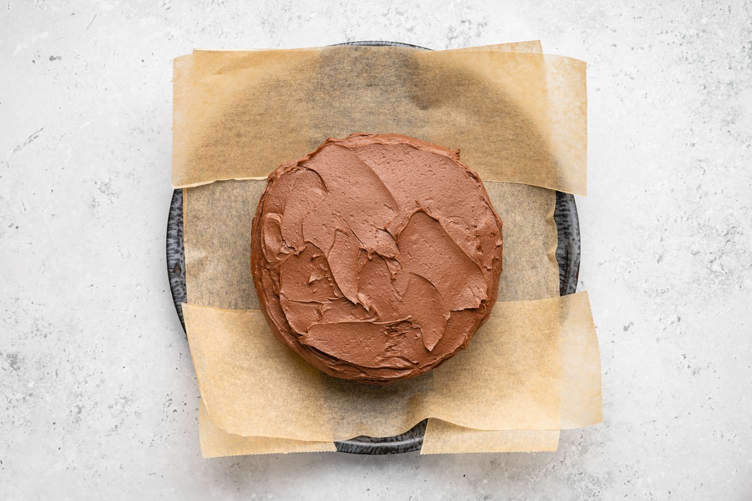 Aerial View of One-Bowl Double-Layer Chocolate Cake on a Parchment Lined Plate With the Icing Smoothened