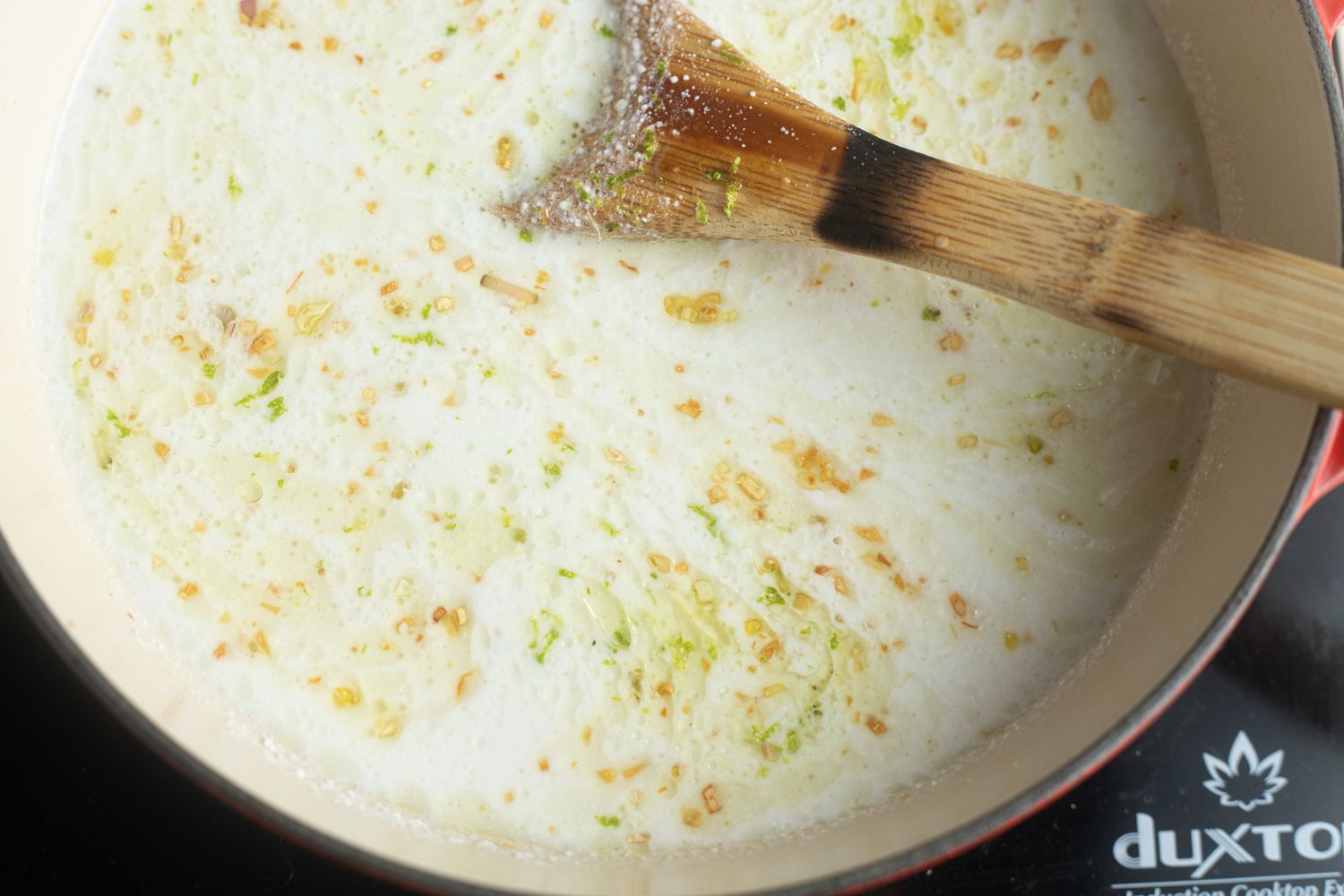Overhead view of a dutch oven with ingredients to make coconut poached fish with bok choy, ginger, and lime