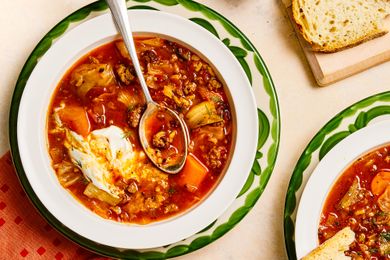 Cabbage roll soup served in a white bowl with a spoon garnished with sour cream surrounded by bread