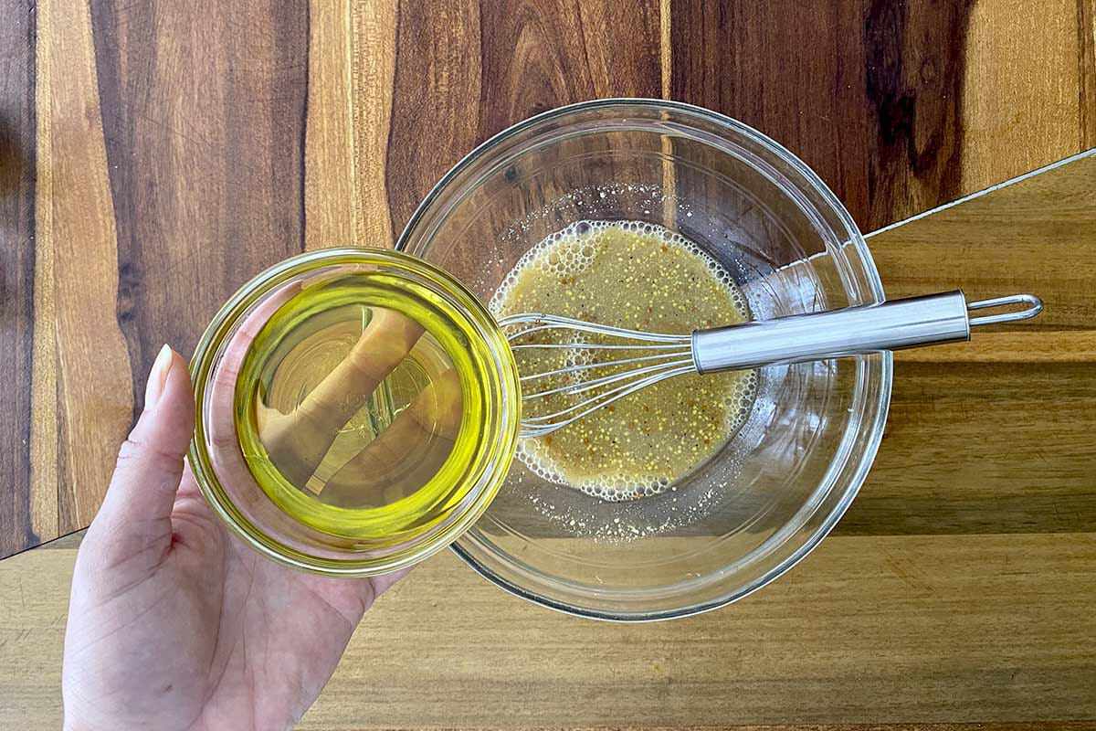 Oil being added to a glass bowl to make the vinaigrette for a Fall Vegetable Salad with Bacon and Maple Dijon Vinaigrette.