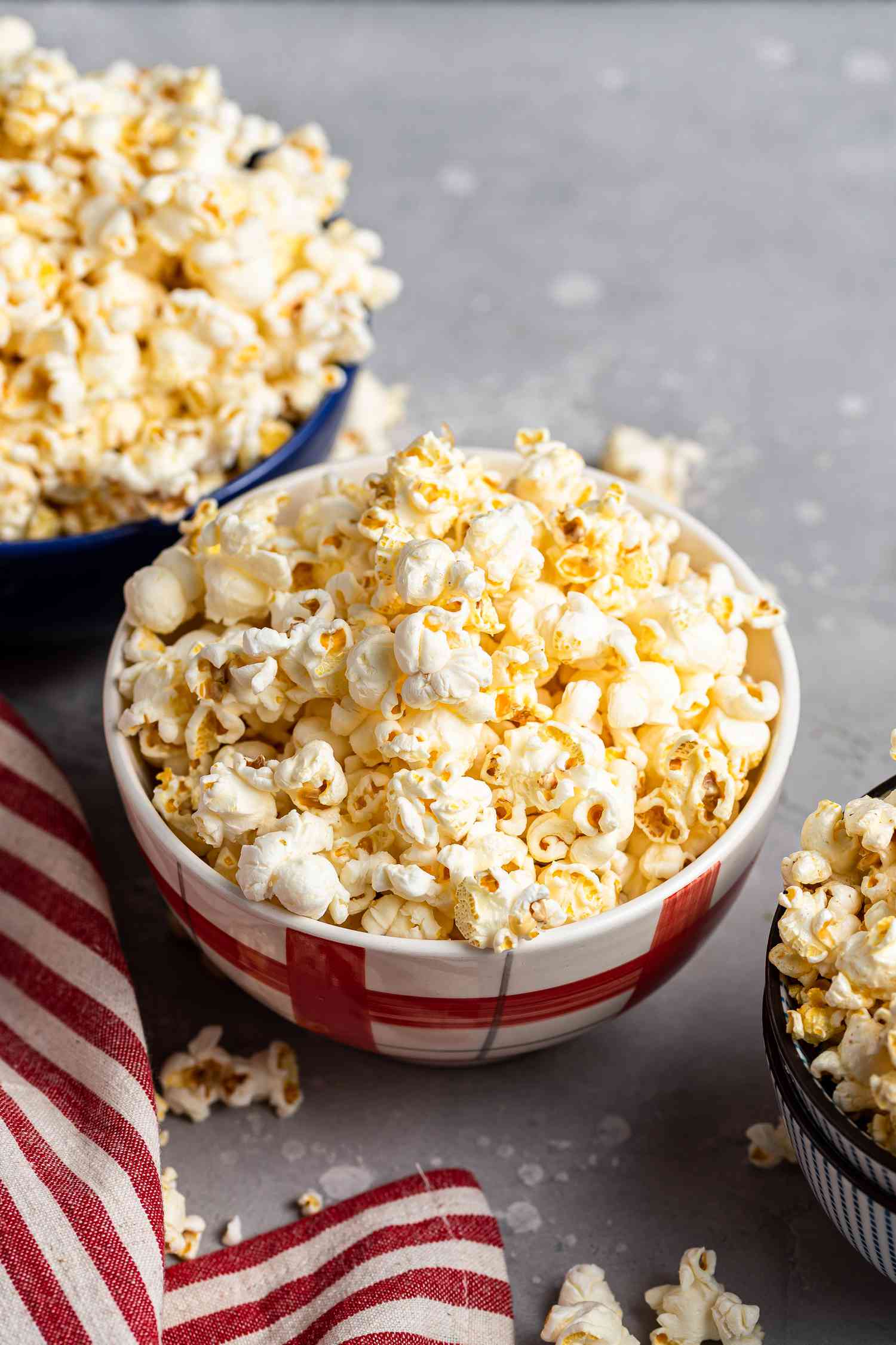 Three bowls filled with popcorn recipes and a red striped linen next to it