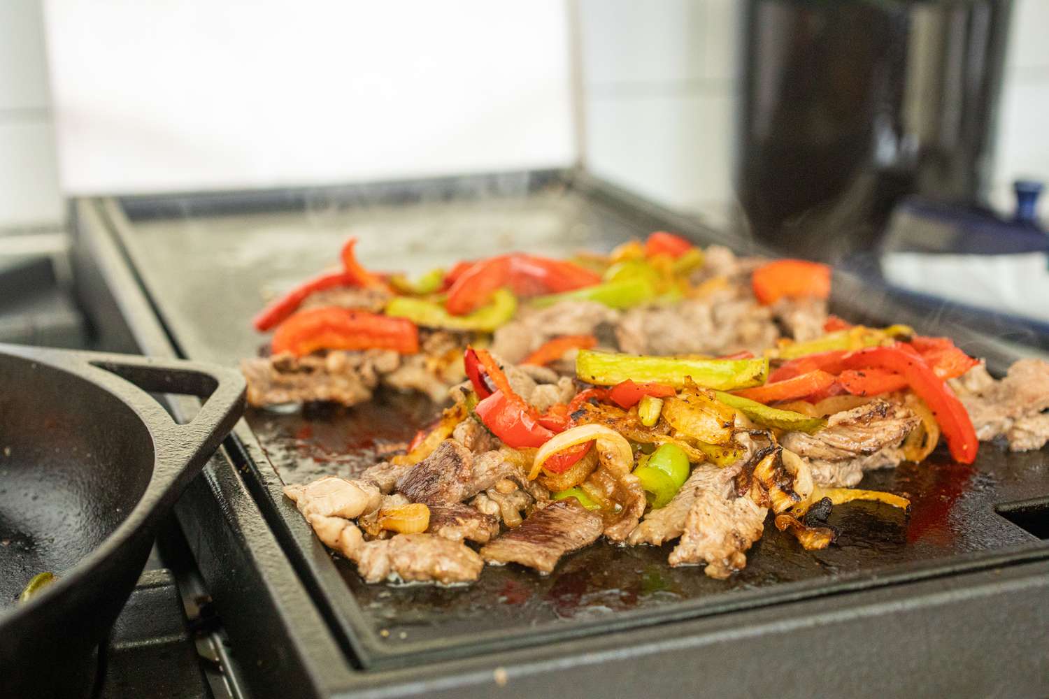 Peppers and beef cooking on a griddle to show how to make a Philly cheesesteak.