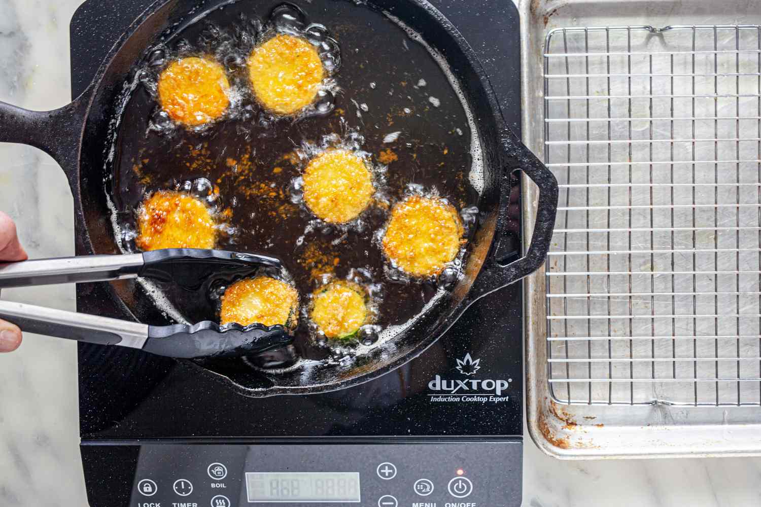 Zucchini Fried in a Cast Iron Skillet with One Piece Being Flipped with Tongs
