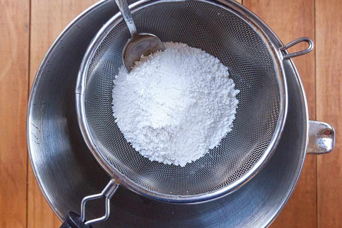 Powdered sugar sifted into the bowl of a stand mixer to show how to make royal icing.