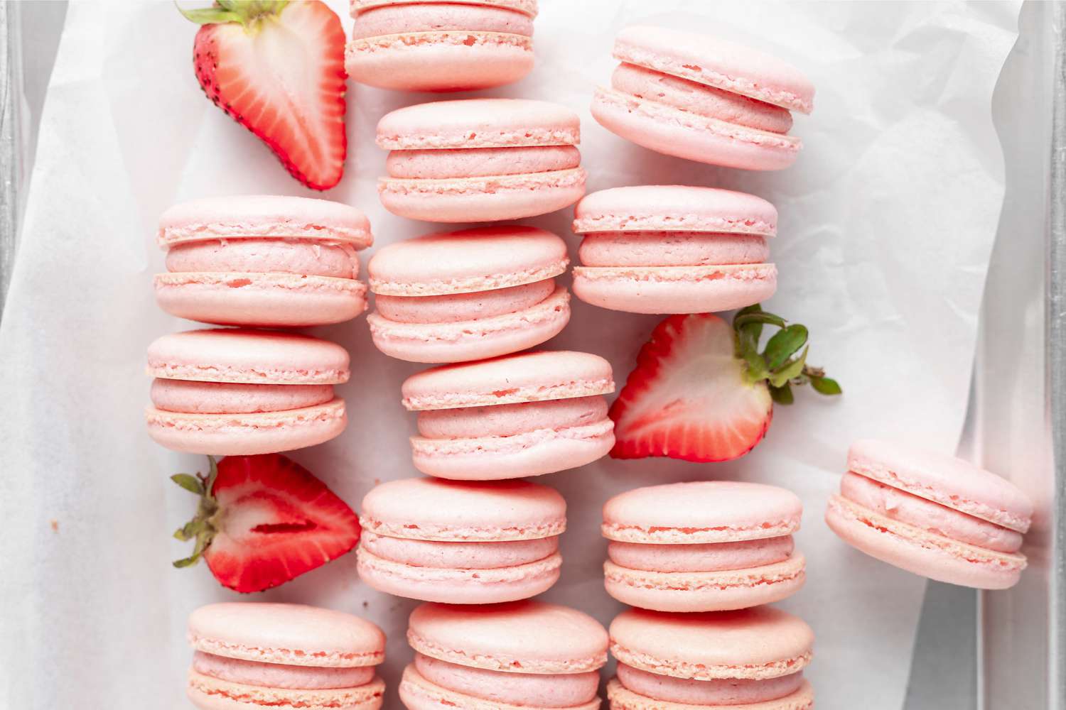 Overhead view of strawberry macarons lined up on their side with halved strawberries set in-between the rows.