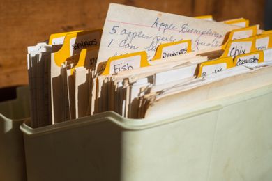 A vintage recipe box filled with handwritten and typed recipe cards organized with tabbed dividers