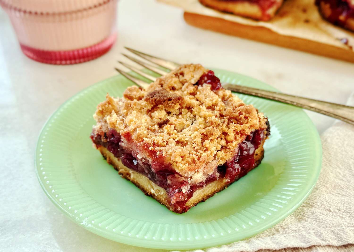 A slice of cherry crumble dessert on a green plate with a fork on the side