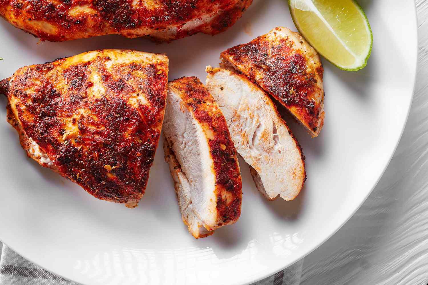 Closeup of a sliced chicken breast on a white plate, with lime wedges for garnish