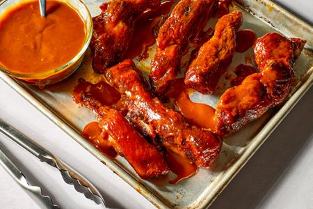 Saucy country-style ribs and a small glass bowl of BBQ sauce with a spoon on a baking sheet pan 