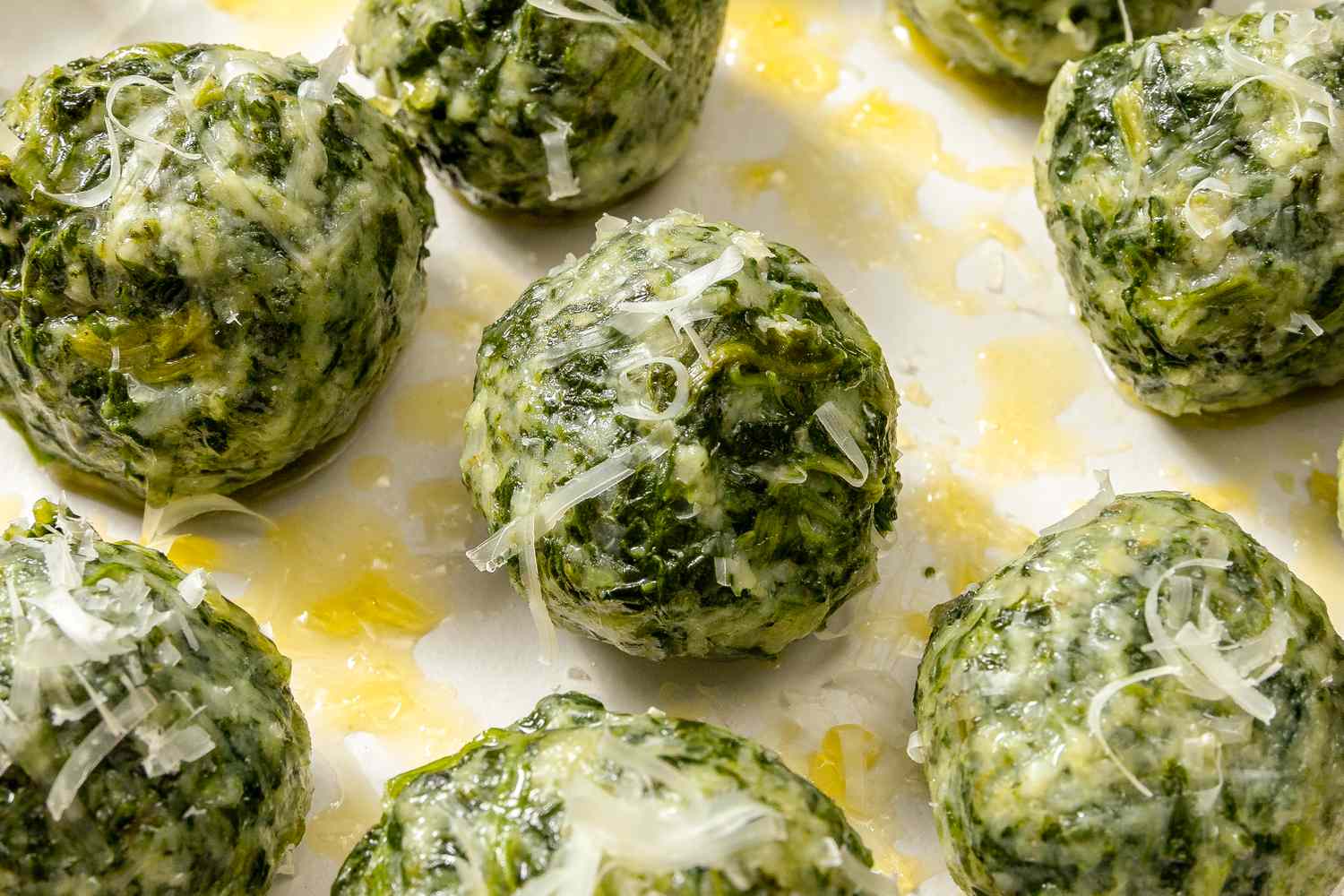 Closeup view of dumplings from Ravioli Gnudi recipe on a white plate with drizzled olive oil