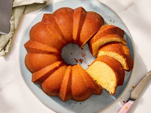 Overhead view of a light blue plate with a partially sliced pound cake next to a cake server and knife on a marble countertop