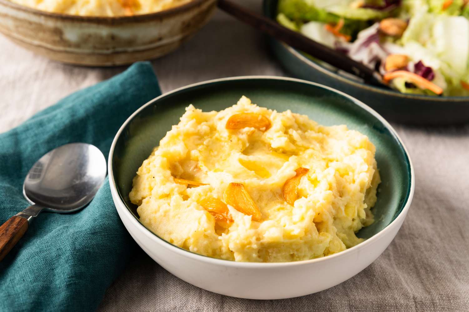 Too Much Garlic Mashed Potatoes in a green and white bowl with a spoon on the side