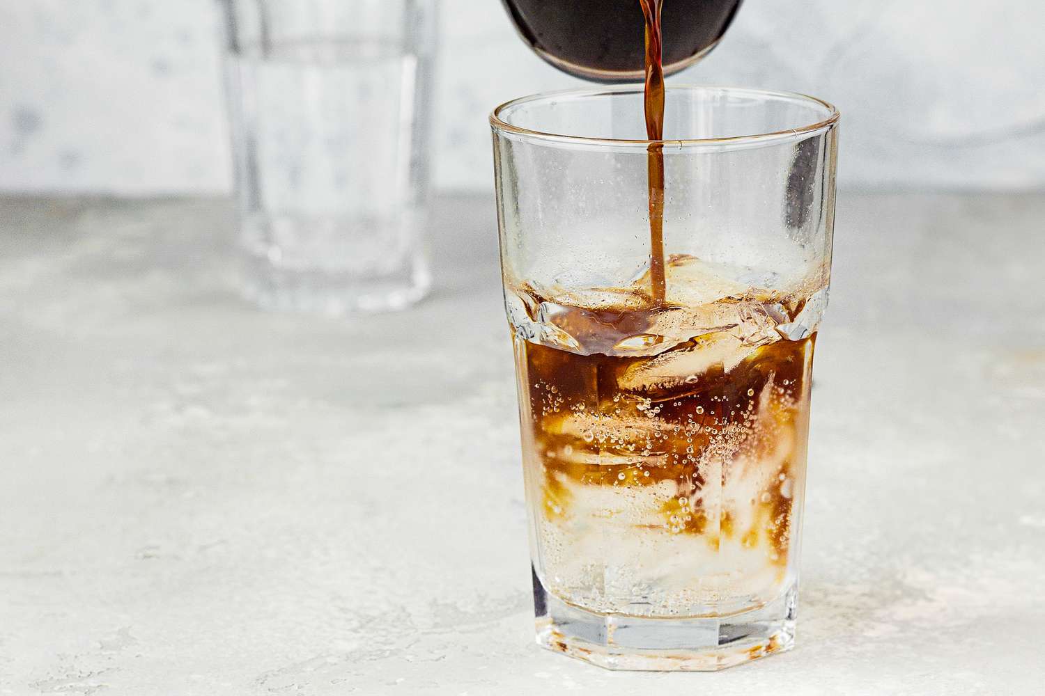 Iced coffee being poured into a glass of seltzer with ice.