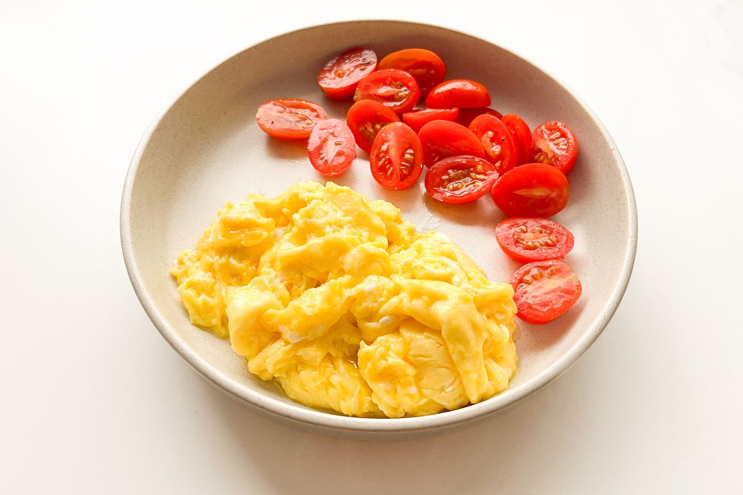 Scrambled eggs and sliced cherry tomatoes arranged on a plate