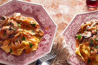 Two plates of beef stroganoff served over wide noodles garnished with herbs