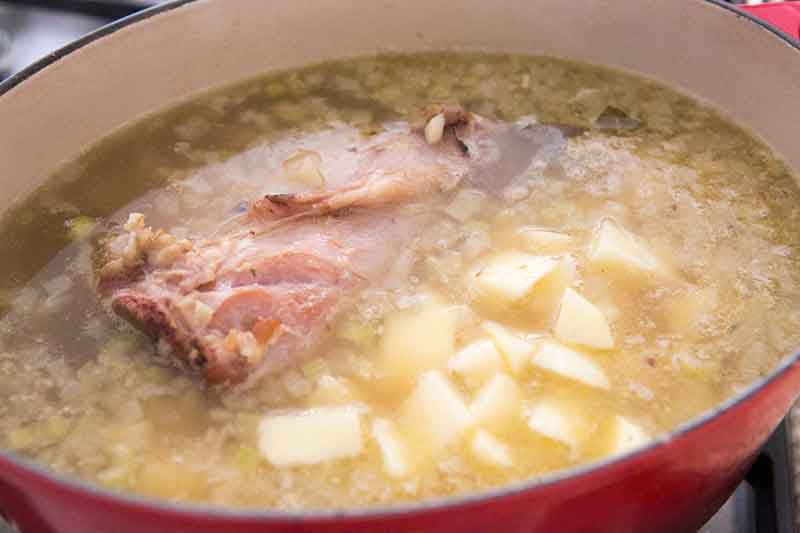 Potato cubes, a ham bone, and garlic cooking in a broth in a pot