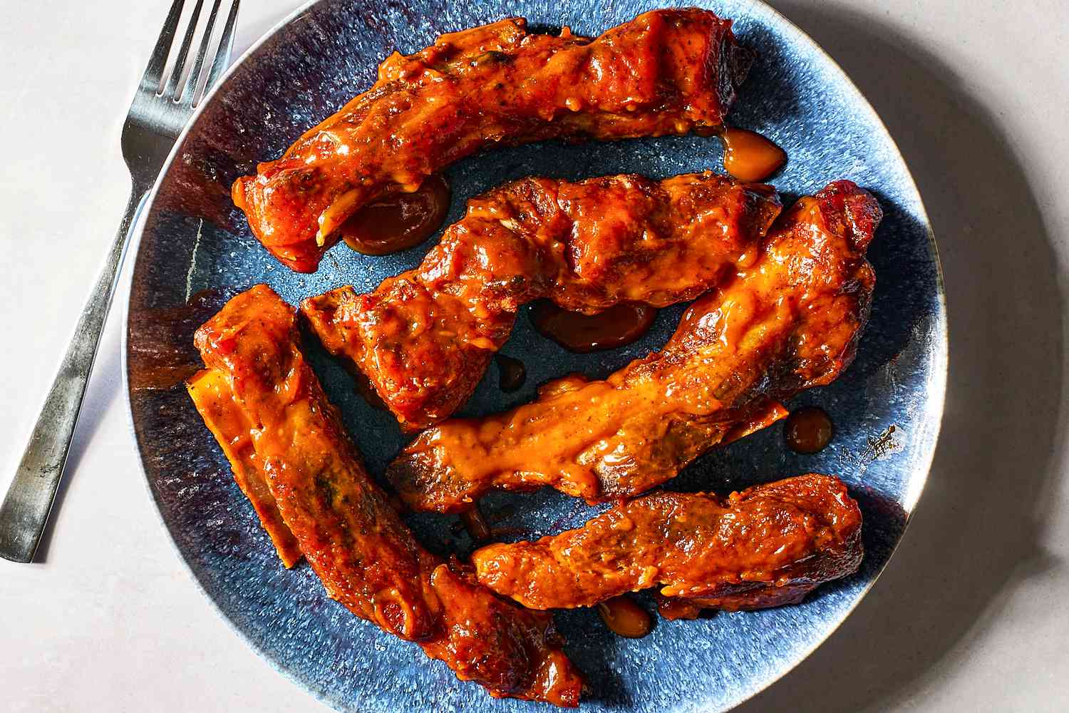 Five saucy country-style ribs on a blue plate, next to a fork