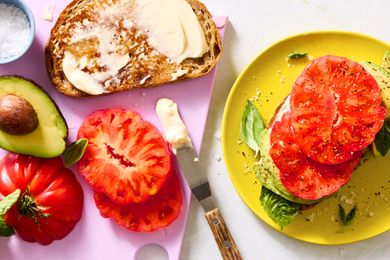 Slices of tomato, bread, avocado, and herbs arranged for sandwiches