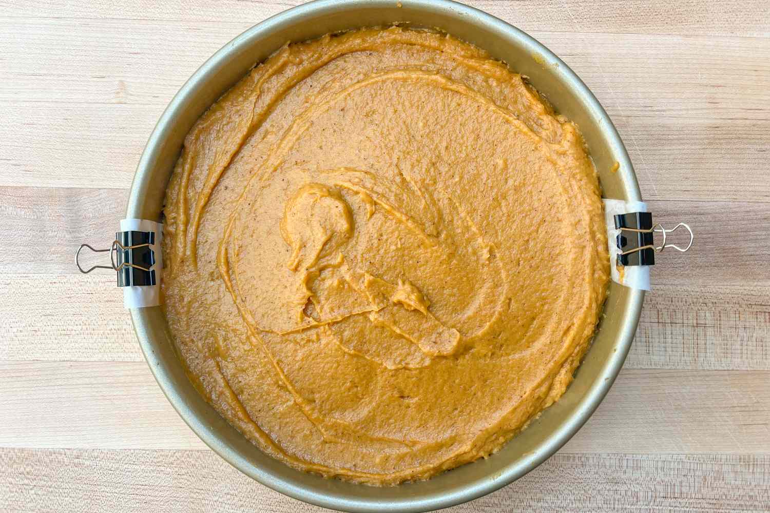 Pumpkin batter in a round cake pan on a wooden surface