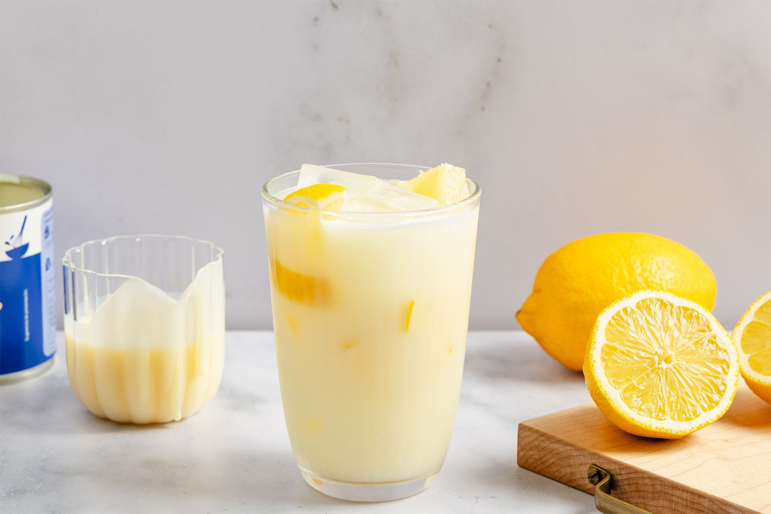 Glass of creamy lemon beverage with a lemon and slices nearby on a table