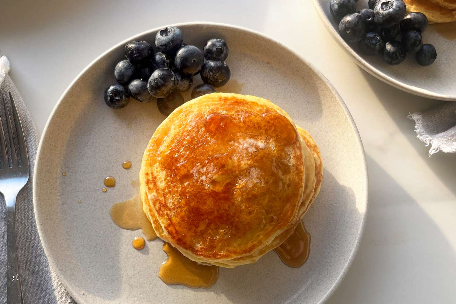 A plate with stacked pancakes drizzled with syrup accompanied by blueberries