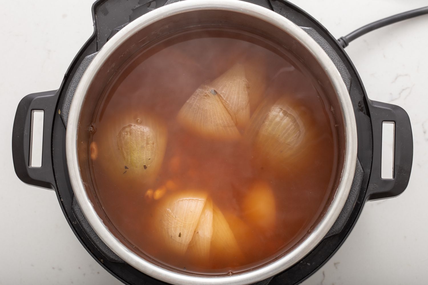 Refried bean ingredients simmering in a pressure cooker.