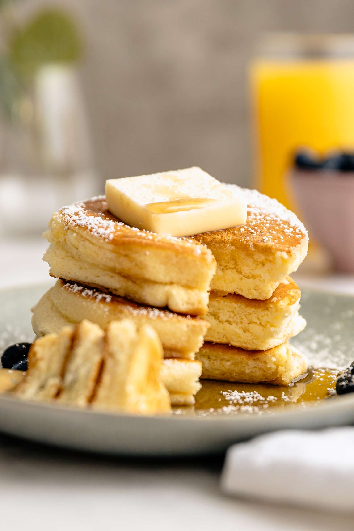 Plate of Japanese Souffle Pancakes Topped with Butter, Maple Syrup, Powdered Sugar, and Blueberries with a Bite Sized Piece Cut Out