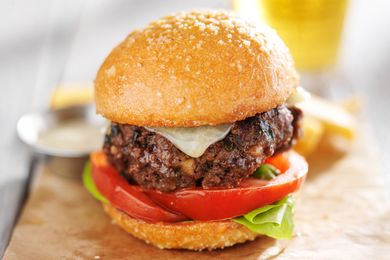 A thick hamburger with lettuce, tomato, and cheese in a bun, placed on a wooden surface with a blurred background