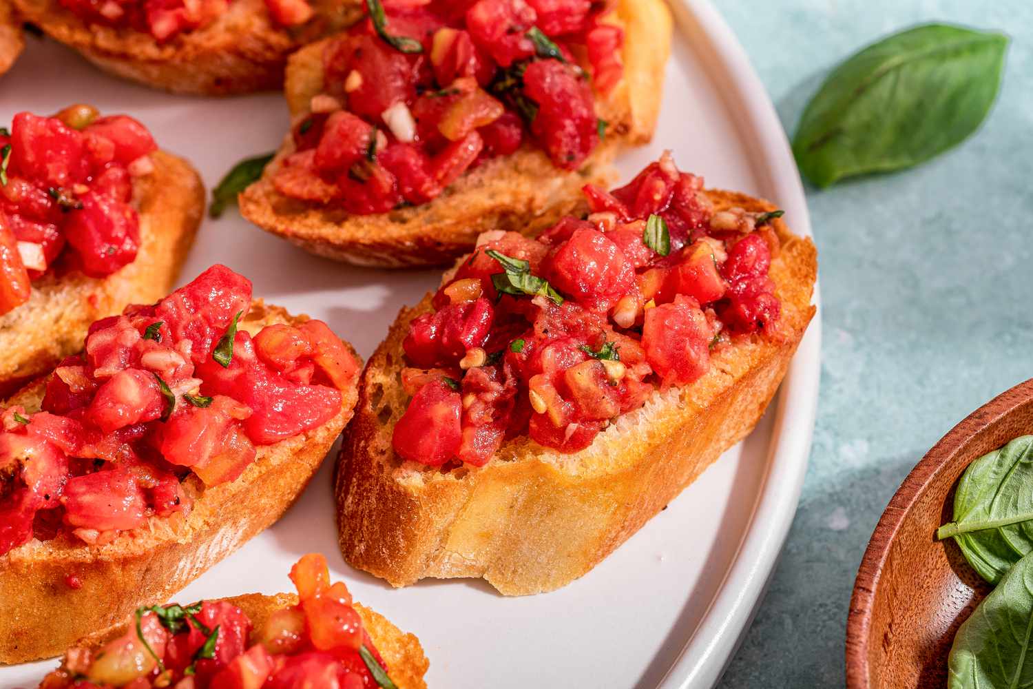 Overhead photo of bruschetta with tomato and basil on a plate and small bowl of basil next to it